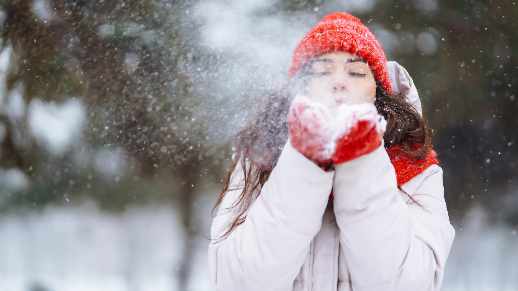 Kvinne i ræd lue og rødt skjerf blåser snø mot kamera