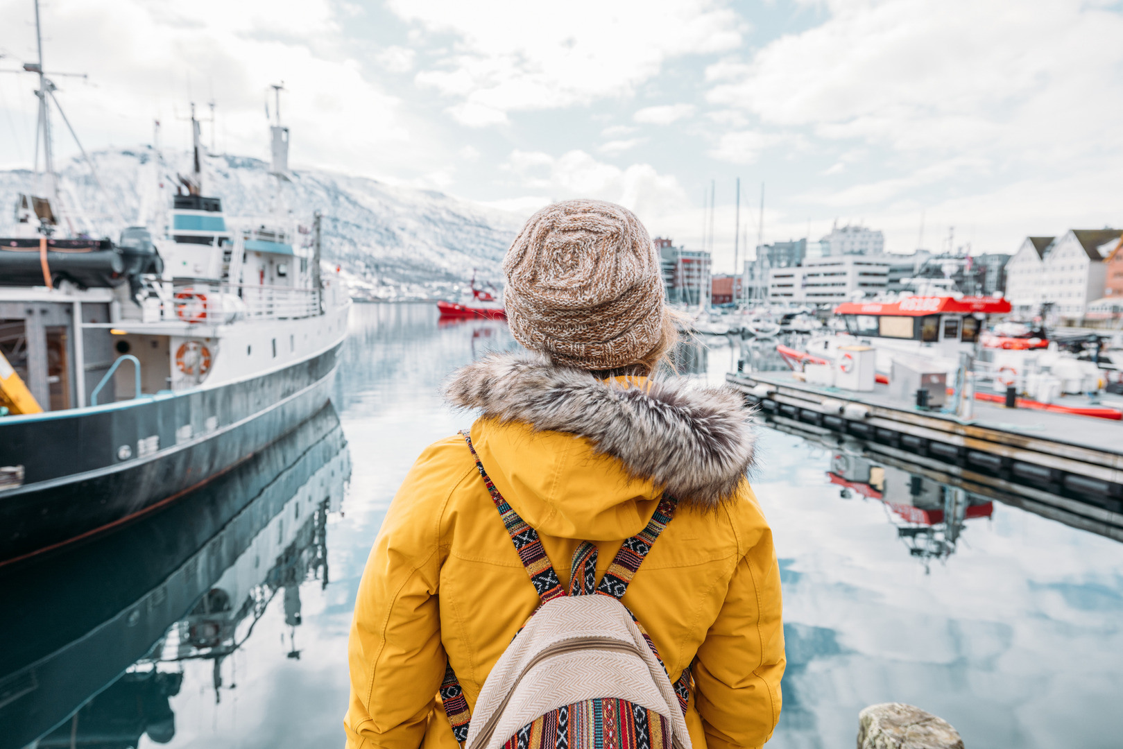 Kvinne med gul jakke ser ut over et fiskehavn i vintervær