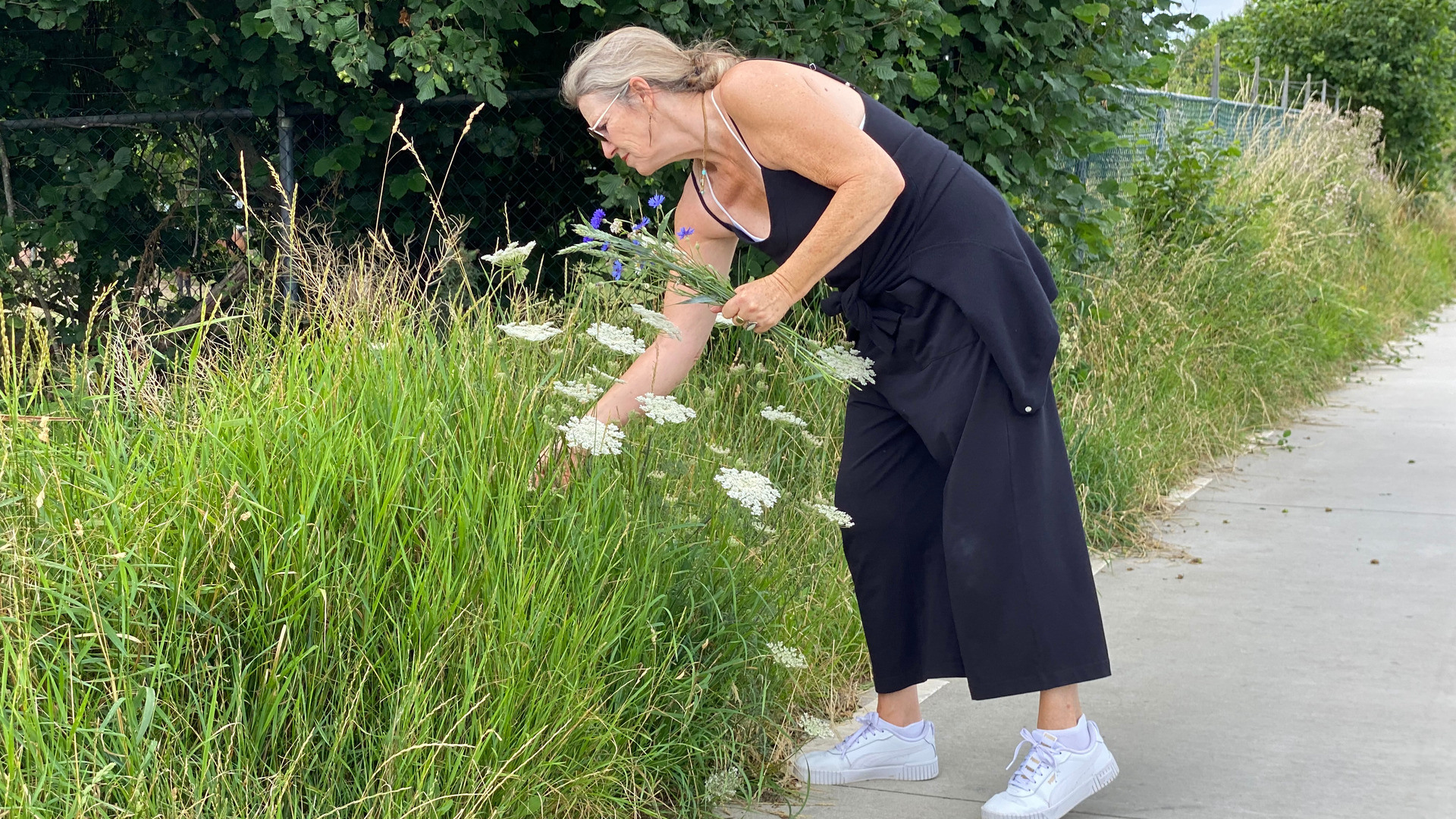 Kvinne i sommerkjole som plukker blomster langs veikanten